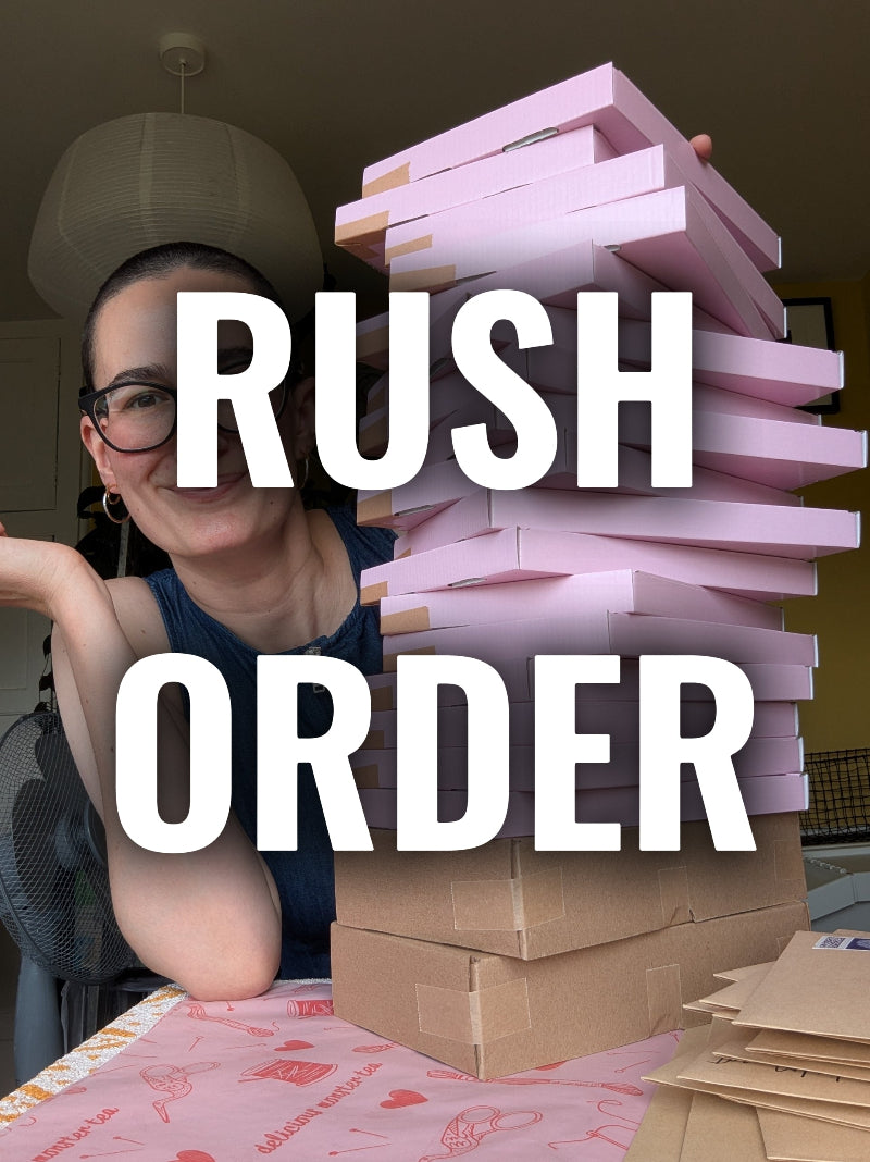 A person behind a stack of pink and brown cardboard boxes with large white text reading 'RUSH ORDER' across the center. The setting appears to be an indoor room with a table and lamp visible in the background.
