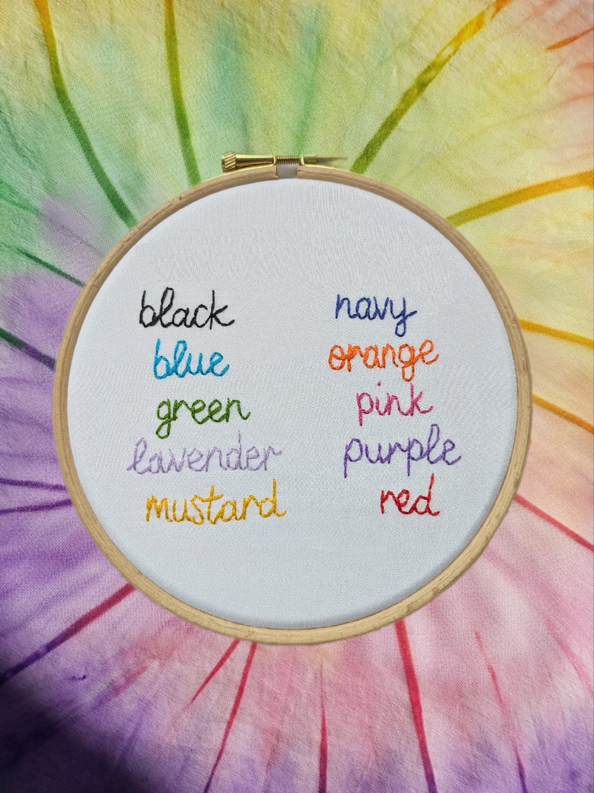Embroidery hoop with color swatch labels on a tie-dye background