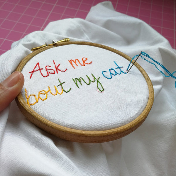 organic cotton white slogan tshirt, embroidered with ask me about my cat in rainbow threads. funny birthday gift for cat mum or cat lover
