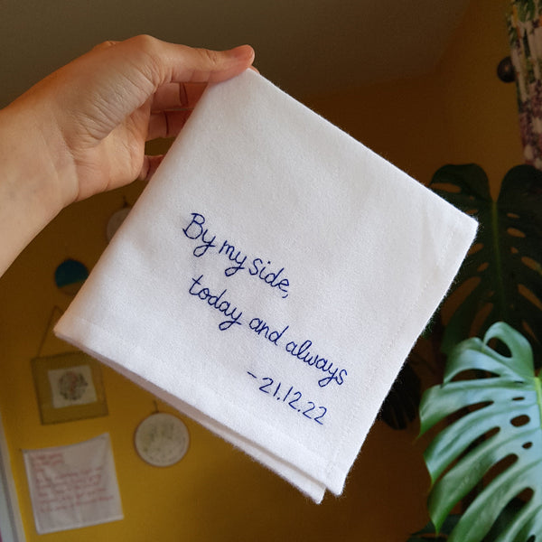 A white cotton handkerchief that is embroidered in navy thread with the message ‘By my side, today and always – 21.12.22'.