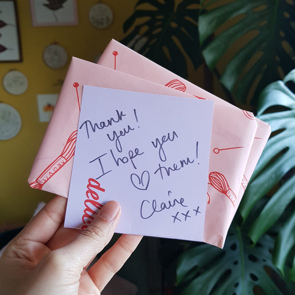 Handwritten note on pink paper with red patterns held by a hand against a colorful background