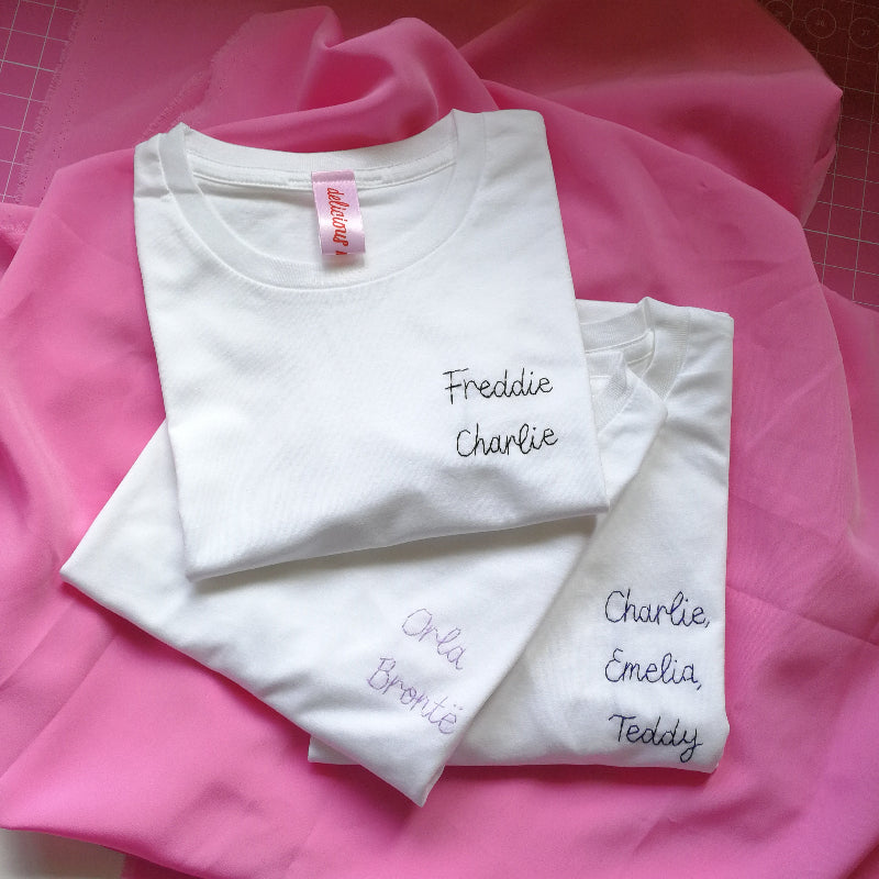 A pile of white cotton t-shirts, all embroidered with children's names.