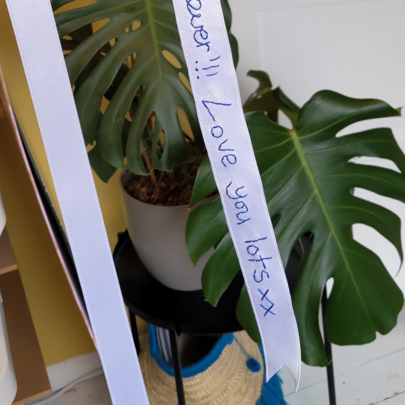 White ribbon with navy handwriting embroidered on it. The embroidery reads 'Love you lots xx'.