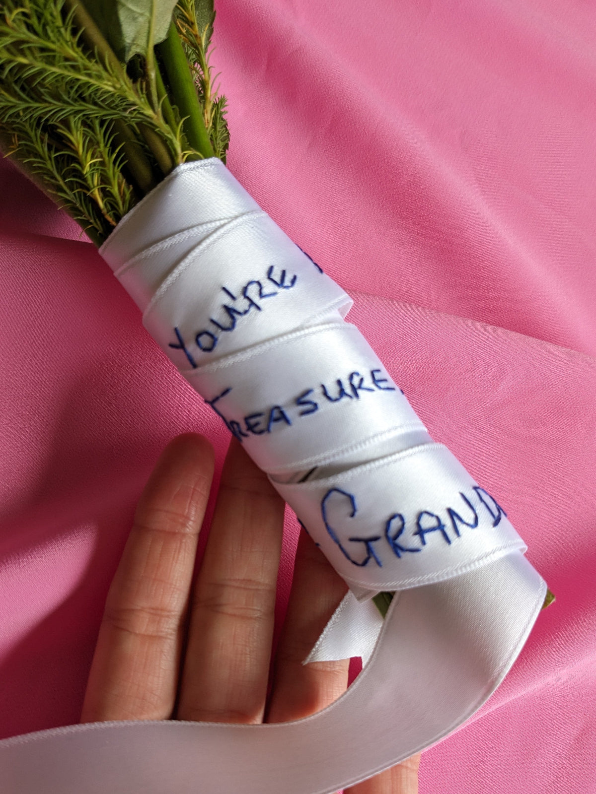 Wedding bouquet wrapped with white personalised ribbon and message on pink fabric