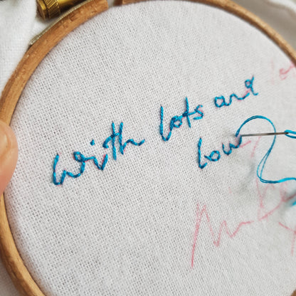 an embroidery hoop with a cotton handkerchief inside being hand embroidered with a handwritten message in blue cotton thread.