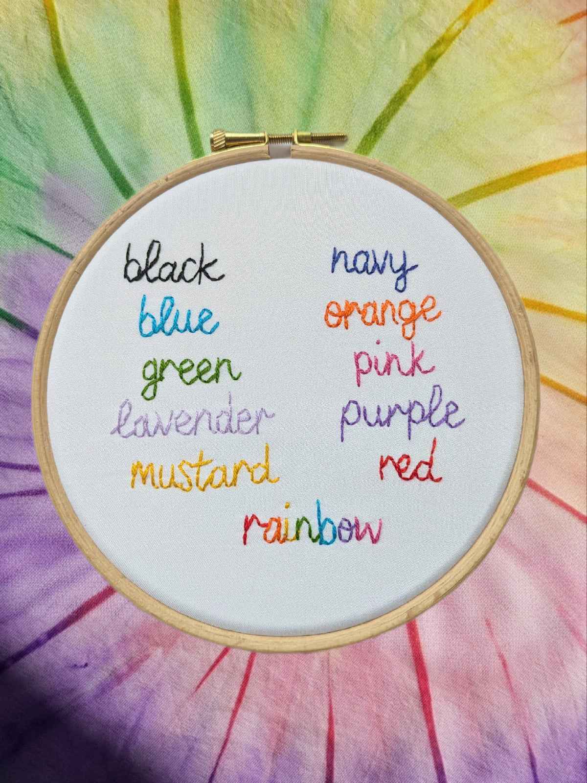 Embroidery hoop with color names in rainbow order on a tie-dye background