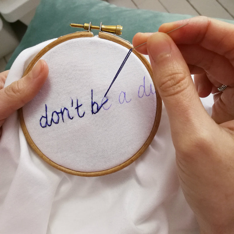 Person embroidering a message on fabric with an embroidery hoop.