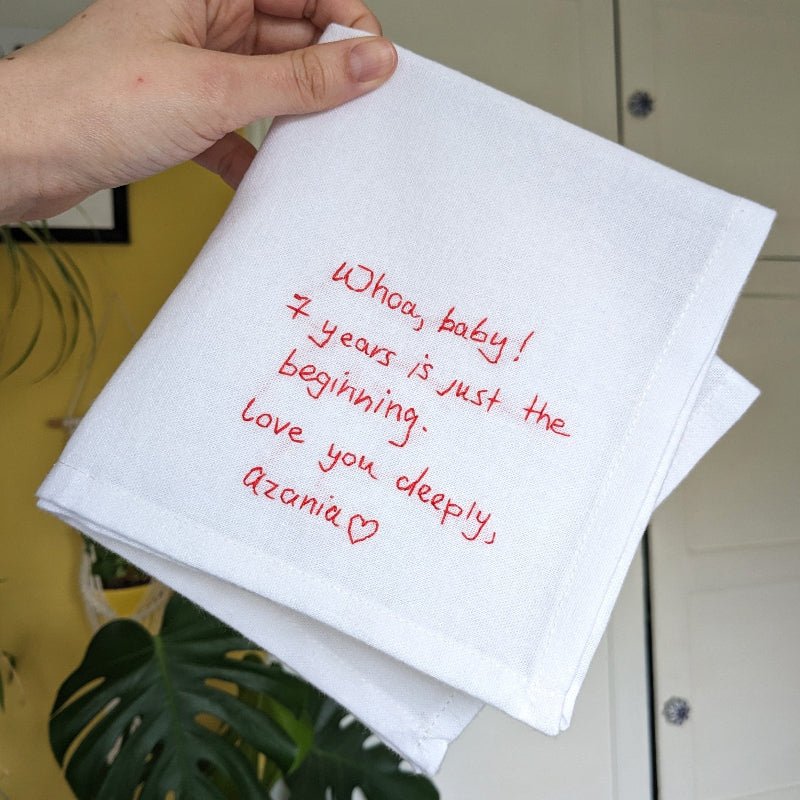 A white cotton handkerchief with red embroidered handwriting that reads 'Whoa, baby! 7 years is just the beginning. Love you deeply, Azonia x'