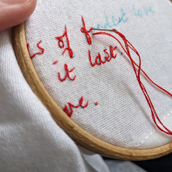 Embroidery hoop with red thread and text on white fabric