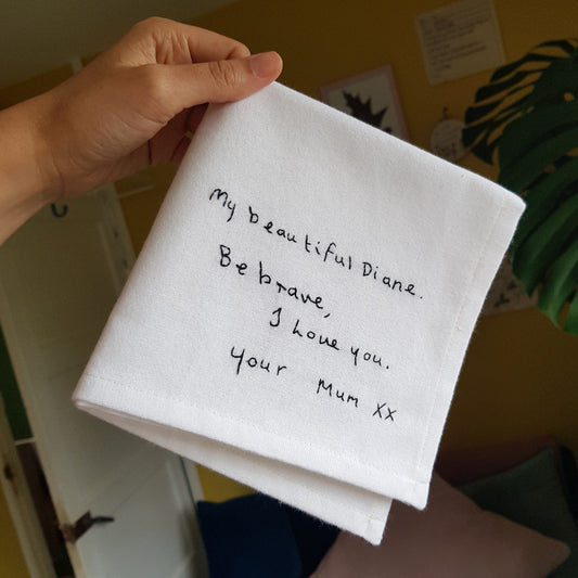 A white cotton handkerchief with black embroidered handwriting that reads 'My beautiful Diane. Be brave, I love you. Your Mum xx'