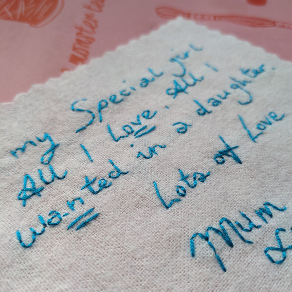 A white cotton wedding dress label with blue embroidered handwriting that reads 'To my special girl, all I love, all I wanted in a daughter. Lots of love Mum xxx'