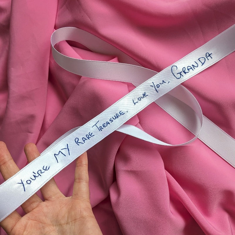 White ribbon with navy handwriting embroidered. The embroidery reads 'You're my rare treasure, love you, Granda'.