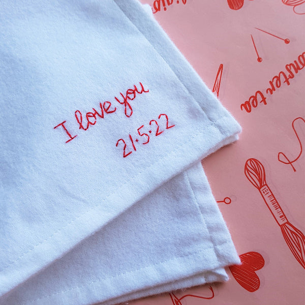 White hanky with 'I love you 21.5.22' embroidery on a pink background with red text and graphics.