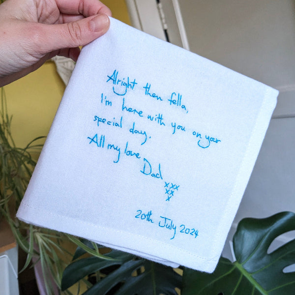 Handwritten message on a white napkin held by a hand, with plants in the background.