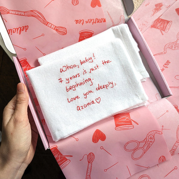 White handkerchief with a romantic message on pink fabric with sewing-themed patterns