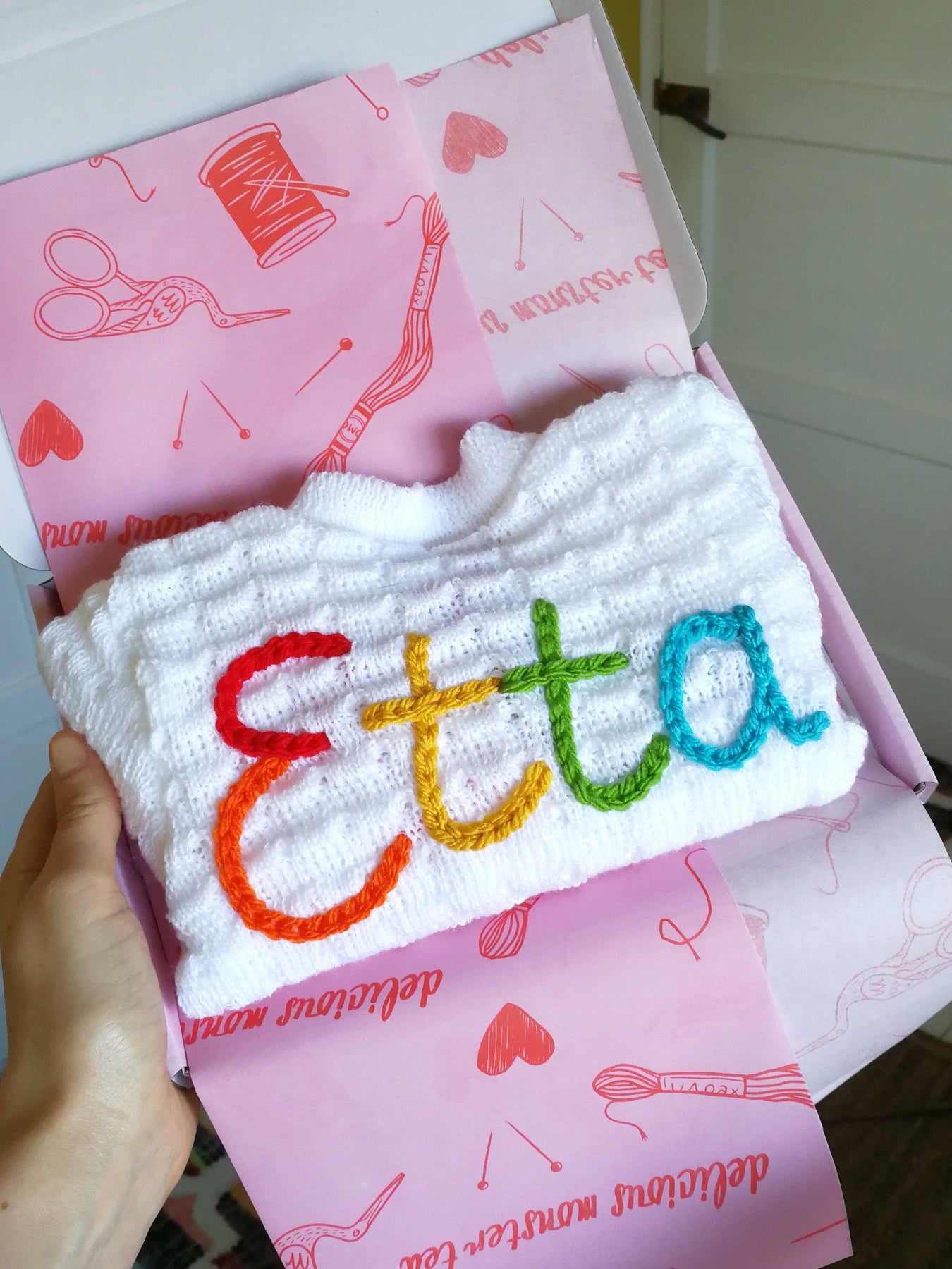 Personalised baby cardigan with colourful hand embroidered name folded in gift box with pink tissue paper