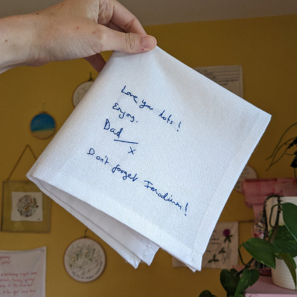 Hand holding a white napkin with blue writing against a yellow wall.