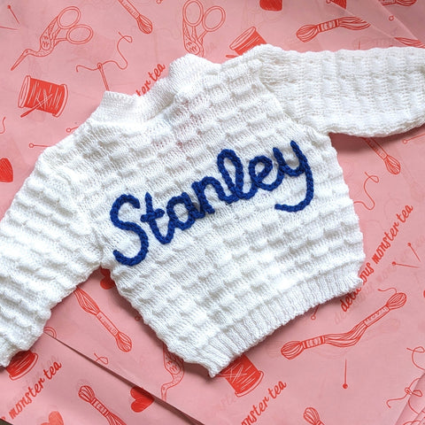 White sweater with 'Stanley' text on a pink patterned surface