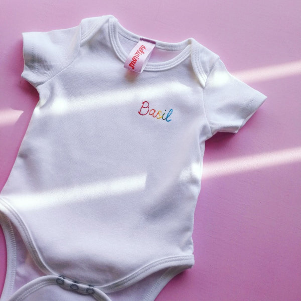 personalised rainbow baby grow, made from white organic cotton, and hand embroidered with baby's name, as a gift for new born baby