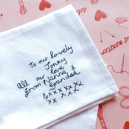 A white cotton handkerchief with black embroidered handwriting that reads 'To our lovely Jonny, all our love from Nanna & Grandad xxxxxx'