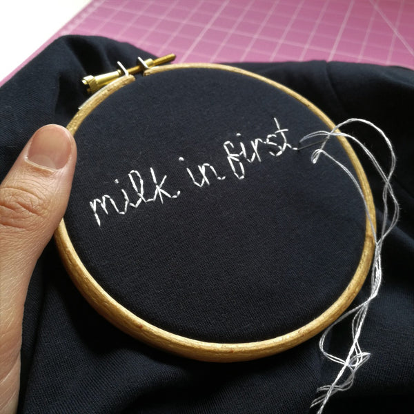 unisex personalised t-shirt, hand embroidered with custom slogan 'milk in first' in white thread, as funny christmas gift or birthday gift for tea lover