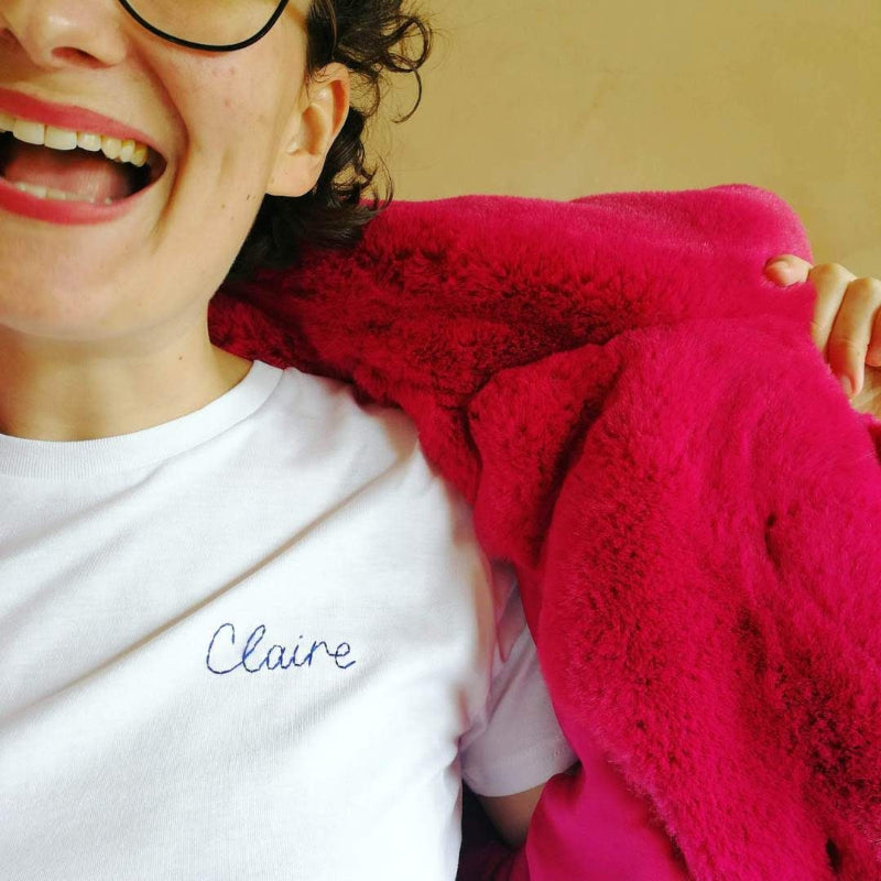 A white woman is wearing a white cotton t-shirt with 'Claire' embroidered on it in navy thread.